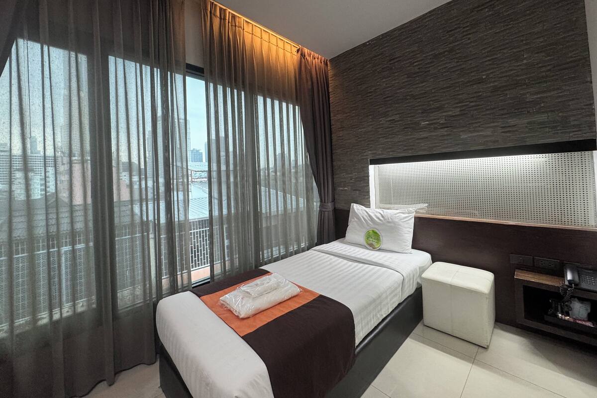 Ein modernes Hotelzimmer mit einem großen Bett, einer kleinen Couch, Blick auf die Stadt und einer Wand in dunklem Holz.