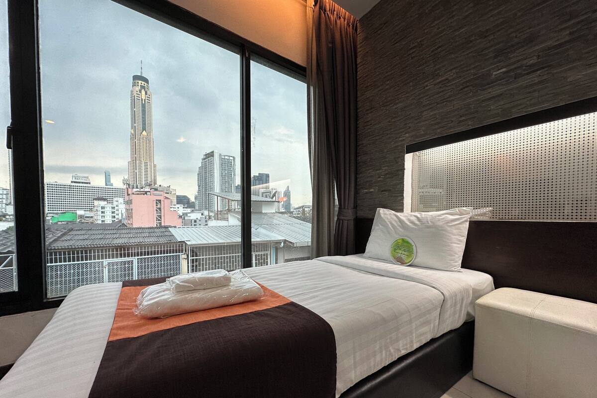 Ein Hotelzimmer mit einem großen Bett, einer Couch und Blick auf die Stadt durch große Fenster.