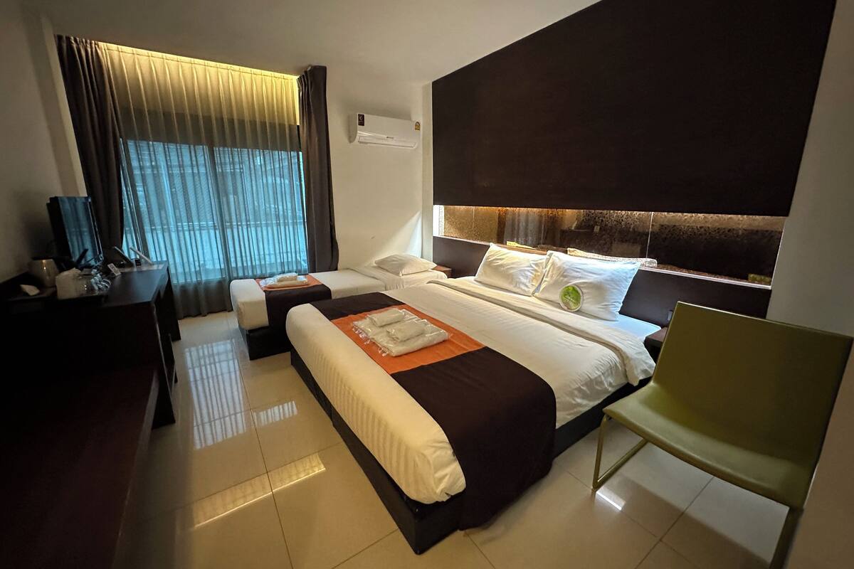 Ein Hotelzimmer mit einem großen Bett, einem kleineren Bett, einem Schreibtisch und einem Stuhl.