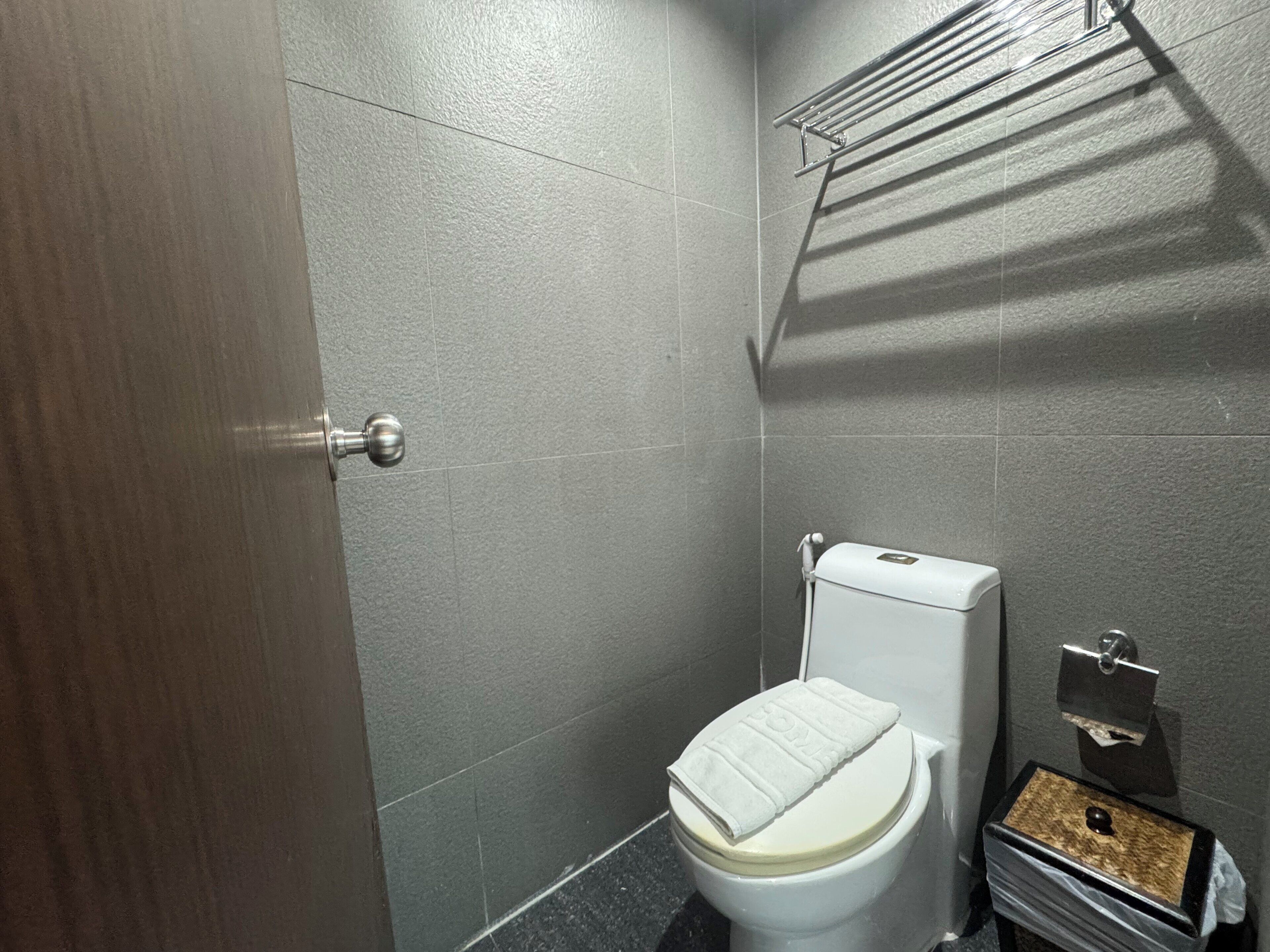 Een badkamer met een toilet, een handdoekhouder en een prullenbak.
