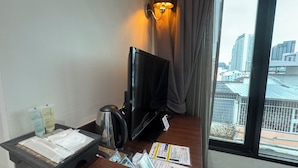 Ein Hotelzimmer mit Schreibtisch, Fernseher, Wasserkocher und einem Fenster mit Blick auf die Stadt.