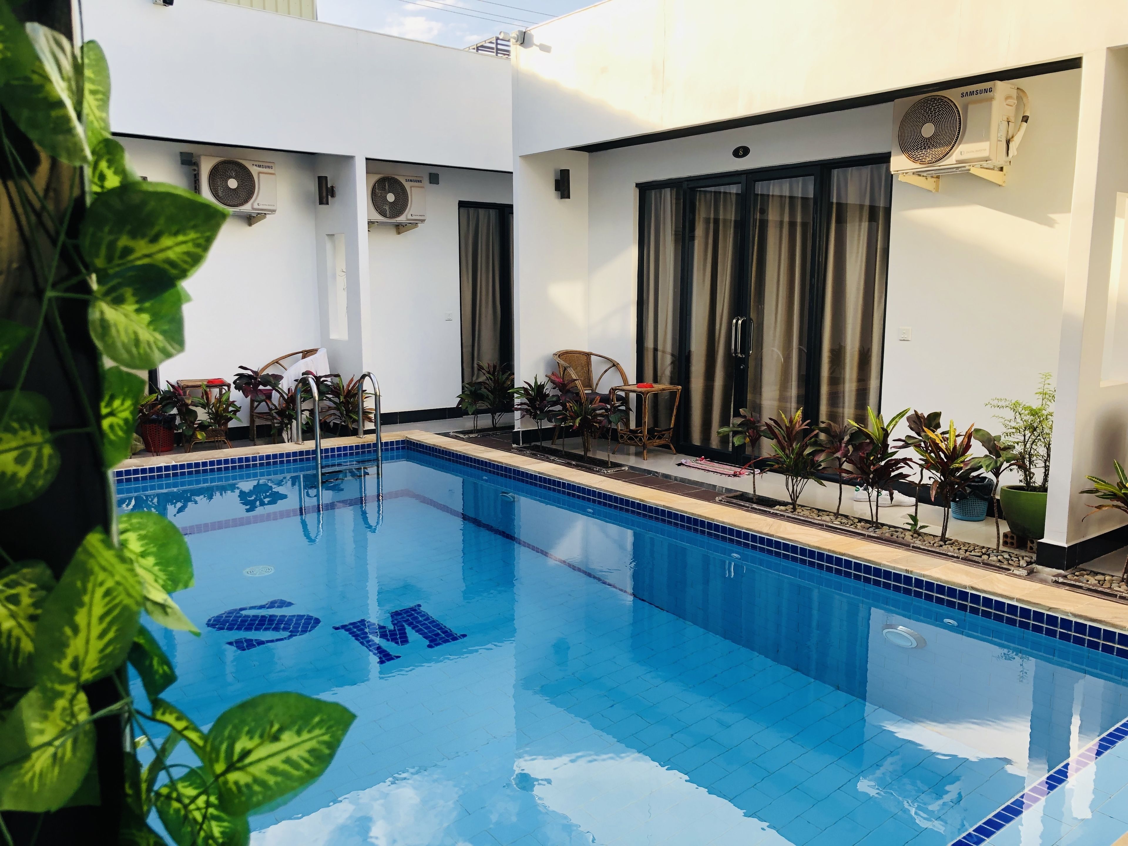 A swimming pool with a tiled edge, surrounded by potted plants and outdoor furniture.