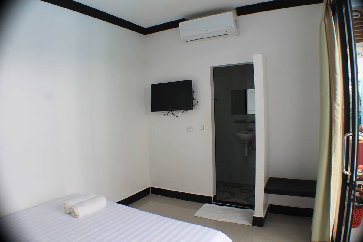 Habitación de hotel con cama, televisor montado en la pared, zona de ducha y un banco.