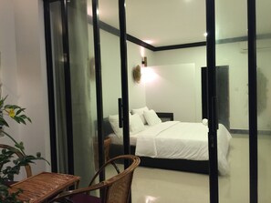 Ein modernes Hotelzimmer mit einer Glastrennwand, einem Bett, einem Sessel und einem kleinen Tisch.