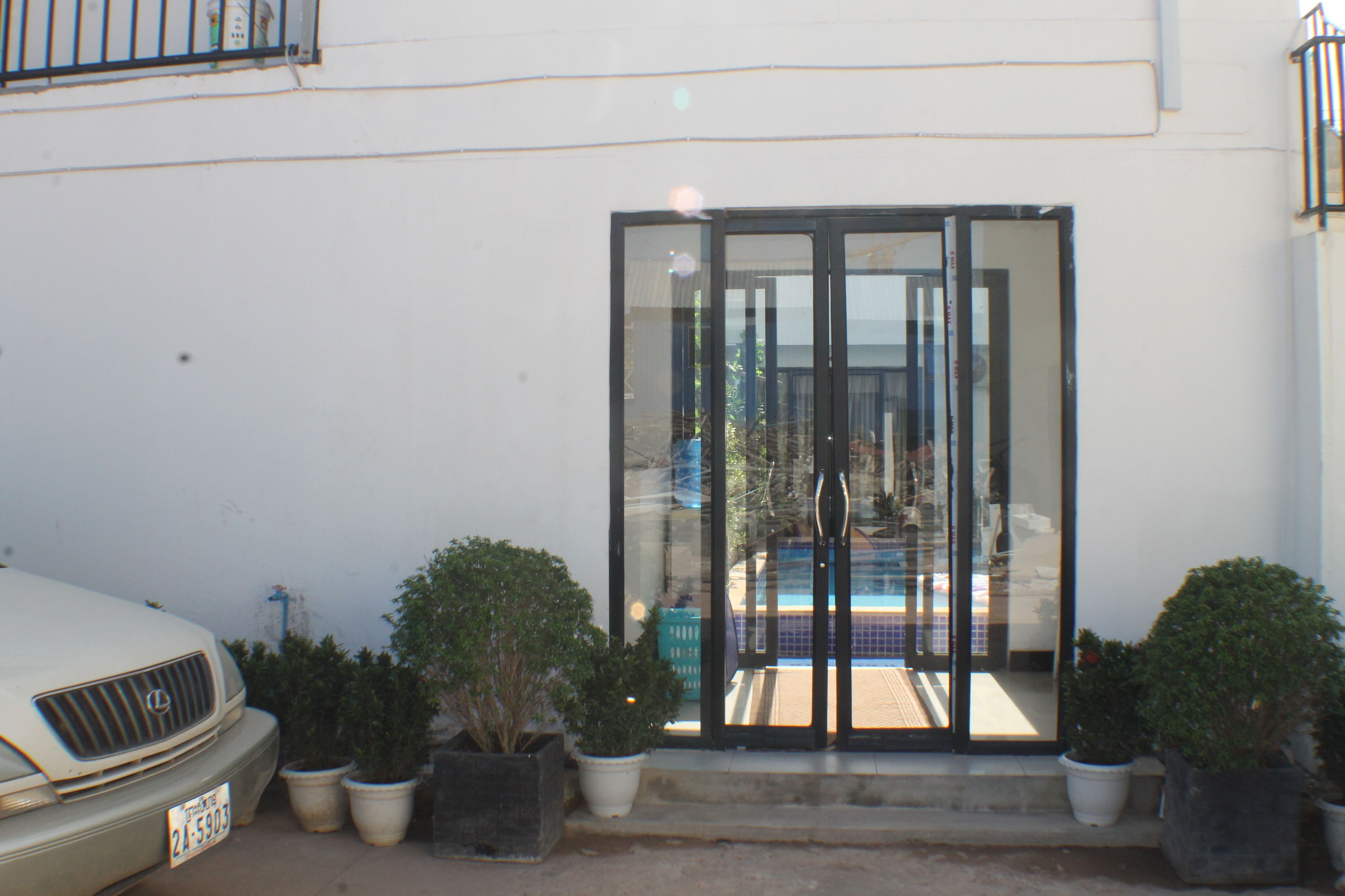 A white building with a glass door entrance, potted plants, and a parked car.