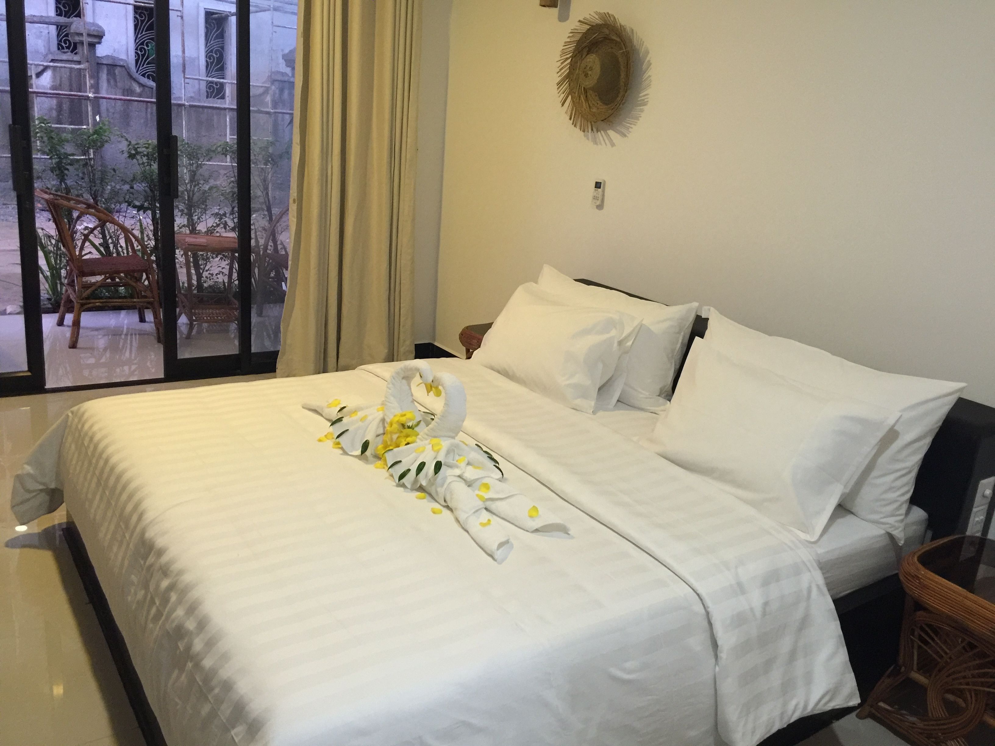 A hotel room with a large bed, a small bedside table, a wall-mounted light, and a view of the outside balcony.