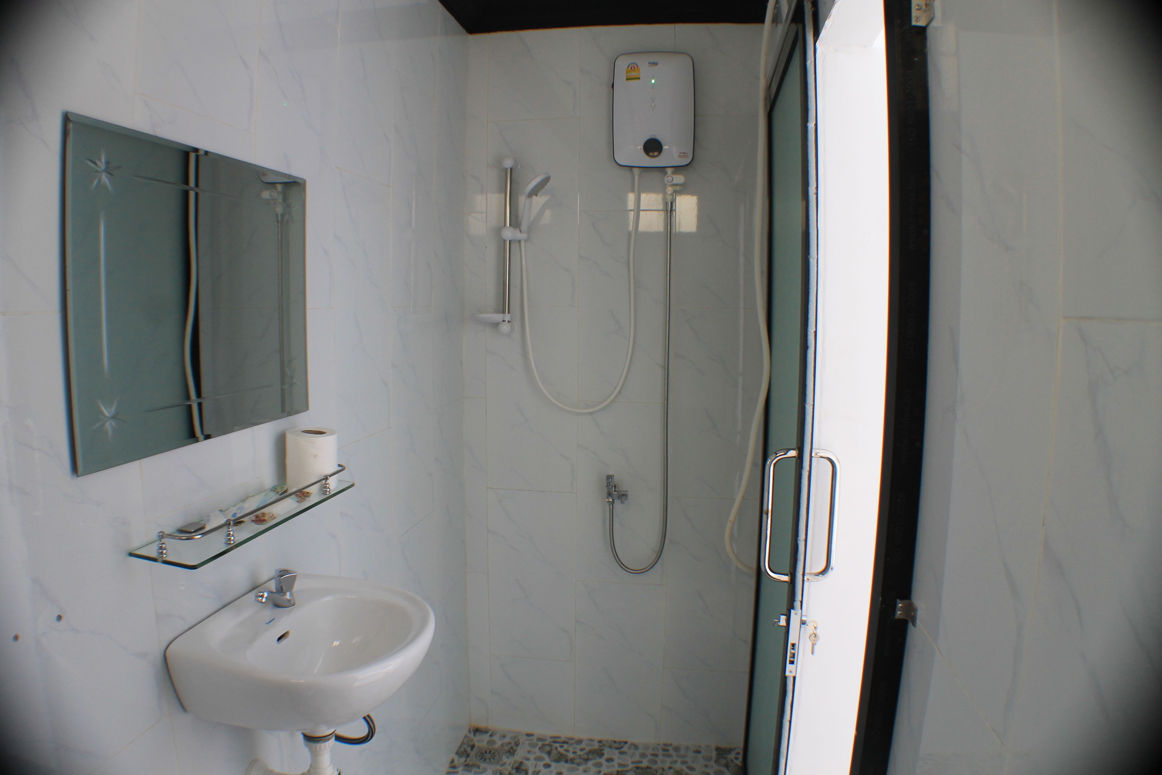 Ein Badezimmer mit Waschbecken, Spiegel, Toilettenpapier, Dusche und einer Glastür.