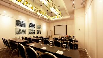 Une salle de conférence avec une longue table, des chaises, un écran de projection et des tableaux accrochés au mur.
