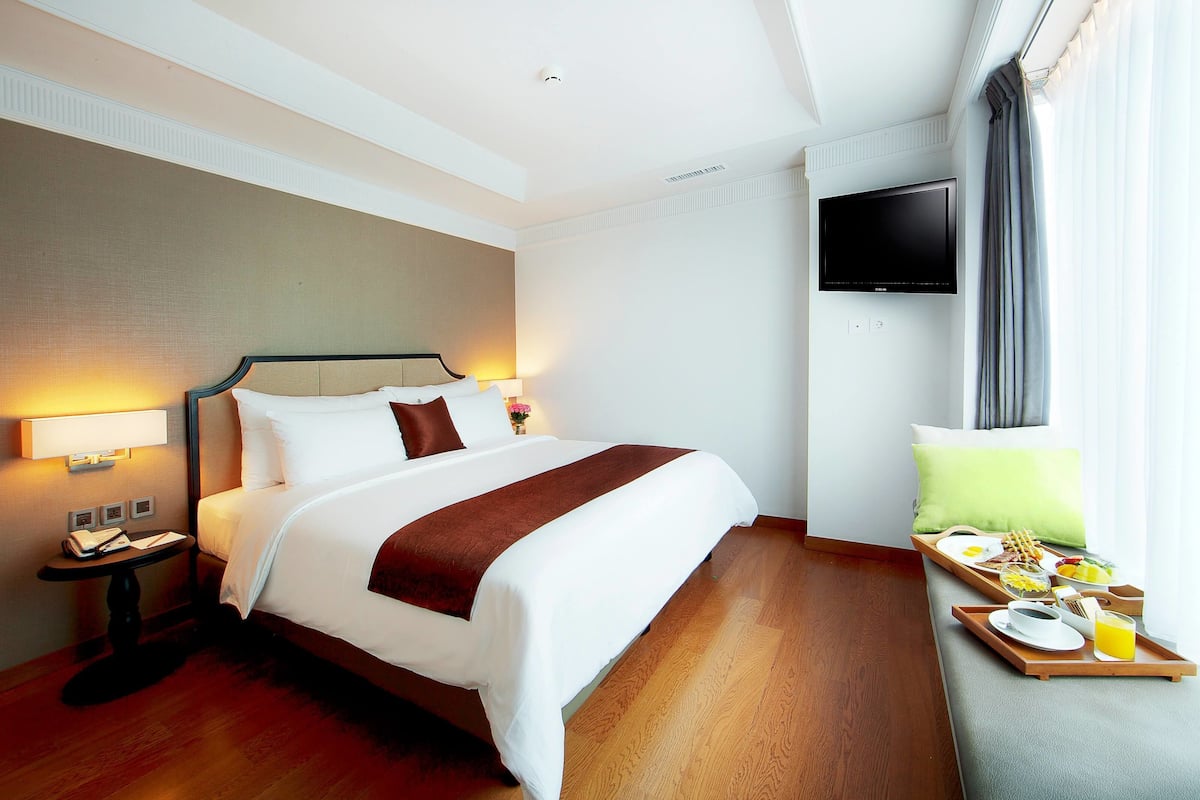 Una habitación de hotel con cama, mesita de noche, televisor y bandeja de desayuno.