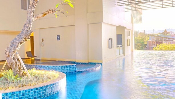Zona de piscina amb un arbre i una cadira, un edifici amb un rètol, i vista d'una construcció llunyana.