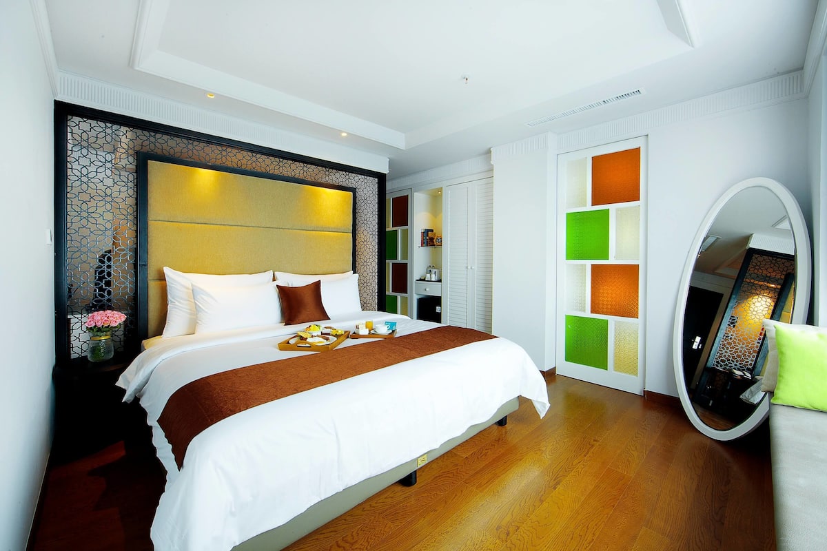 Una habitación de hotel moderna con una cama grande, una mesita de noche con un florero y un espejo con un marco decorativo.