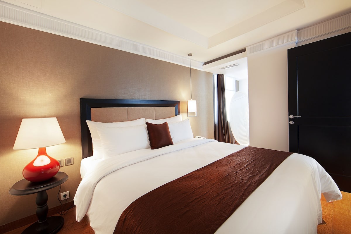 Una habitación de hotel con una cama grande, una mesita de noche con una lámpara y una puerta.