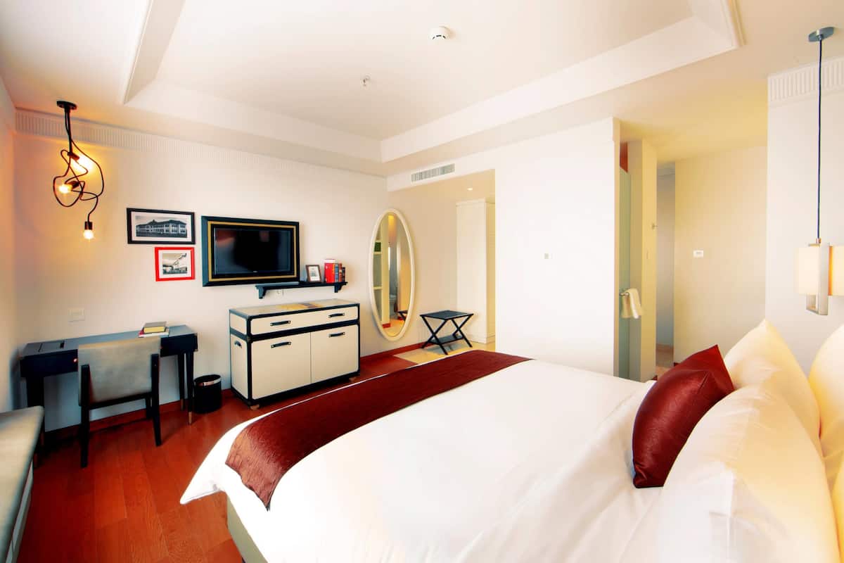 Una habitación de hotel con cama, escritorio, televisor, espejo y una pared decorada en rojo.