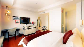A hotel room with a bed, a desk, a television, a mirror, and a red accent wall.