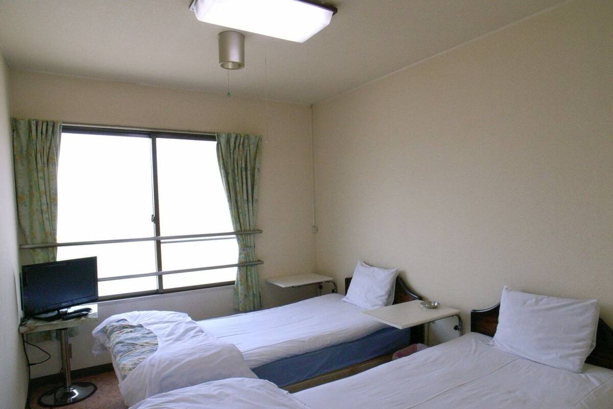 Ett hotellrum med två separata sängar, ett skrivbord med en dator och ett fönster med gardiner.