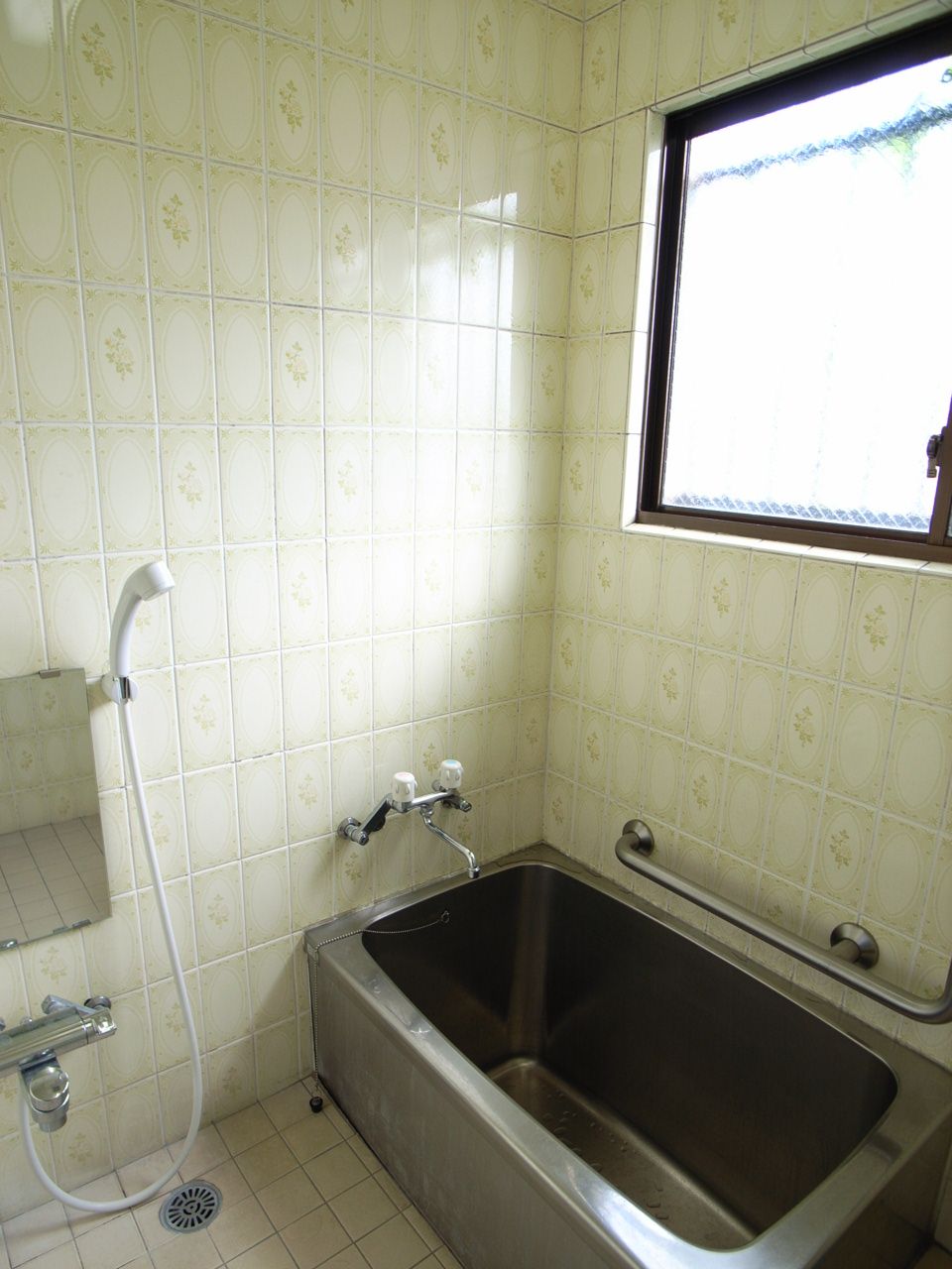 A bathroom with a bathtub, a showerhead, and a window.