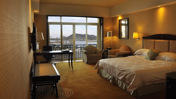 A hotel room with a bed, desk, chairs, and a view of a body of water. - Anqing Country Garden Phoenix Hotel (Anqing)