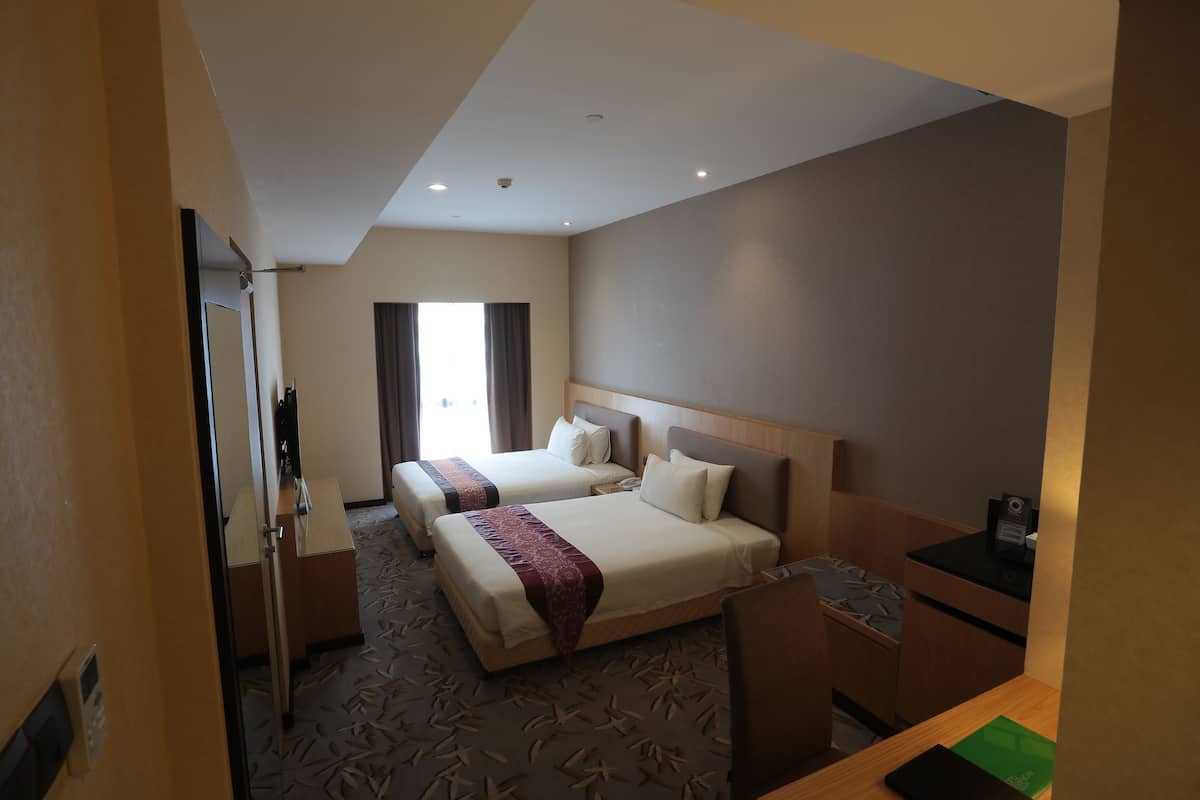 Ein Hotelzimmer mit zwei Betten, einem Schreibtisch, einem Stuhl, einem kleinen Tisch und einem Fenster mit Vorhängen.