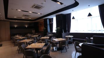 A modern dining area with tables and chairs, large windows, and a ceiling with recessed lighting.