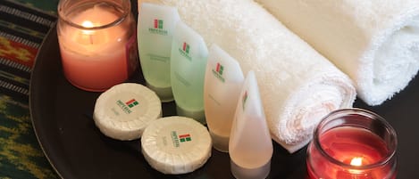 A tray with a lit candle, a rolled towel, and various toiletries including soap and shampoo.