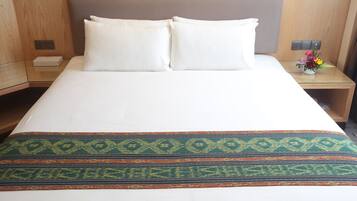 Una habitación de hotel con una cama grande, dos almohadas, una mesita de noche con un jarrón de flores y un cabecero de madera.