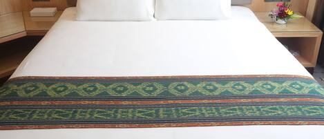A hotel room with a large bed, two pillows, a nightstand with a vase of flowers, and a wooden headboard.