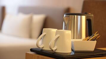 A wooden table with two white mugs, a stainless steel coffee pot, and a white bowl with pens and pencils.