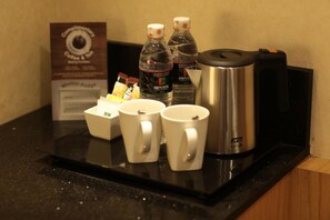 Un coin café comprenant une machine à café, deux bouteilles d’eau et trois tasses blanches posées sur un comptoir noir.