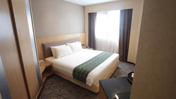 Habitación de hotel con una cama grande, una mesita de noche, un escritorio y una ventana con cortinas.