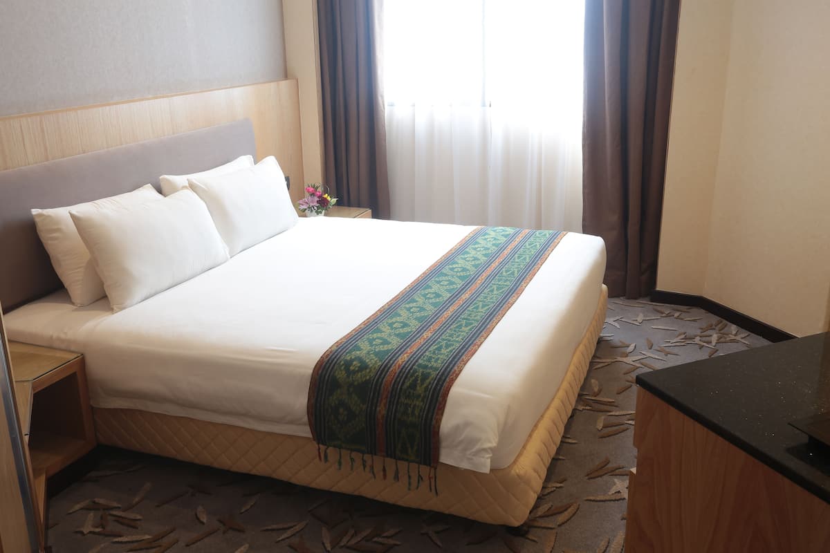 Ein Hotelzimmer mit einem großen Bett, einem Holzkopfteil, einem Nachttisch und einem Schreibtisch.