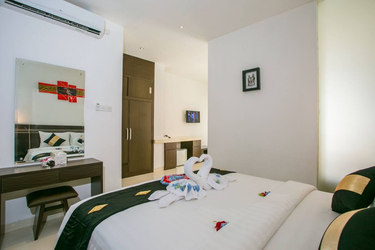 A hotel room with a bed, a desk, a mirror, a wardrobe, and a small TV.