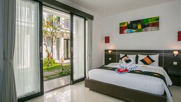 A hotel room with a large bed, a sliding glass door to a garden, and a painting on the wall.