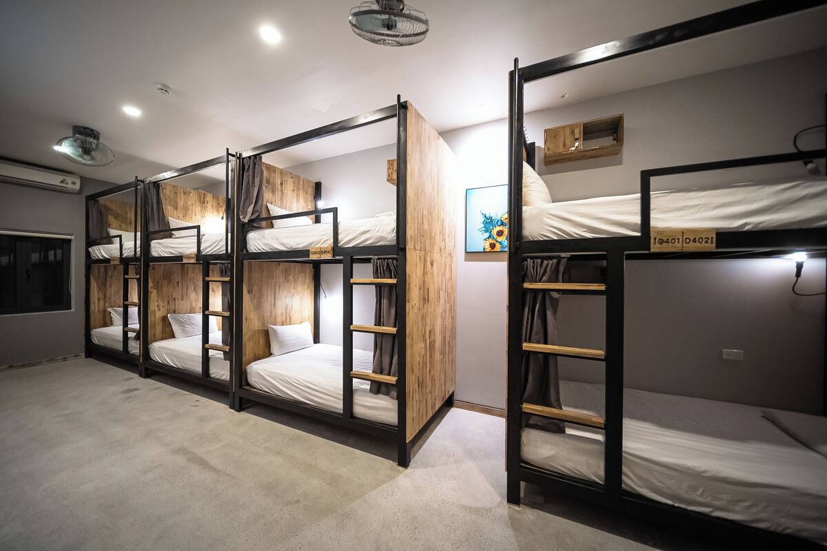 A dormitory room with bunk beds, a ceiling fan, and a small wooden cabinet.