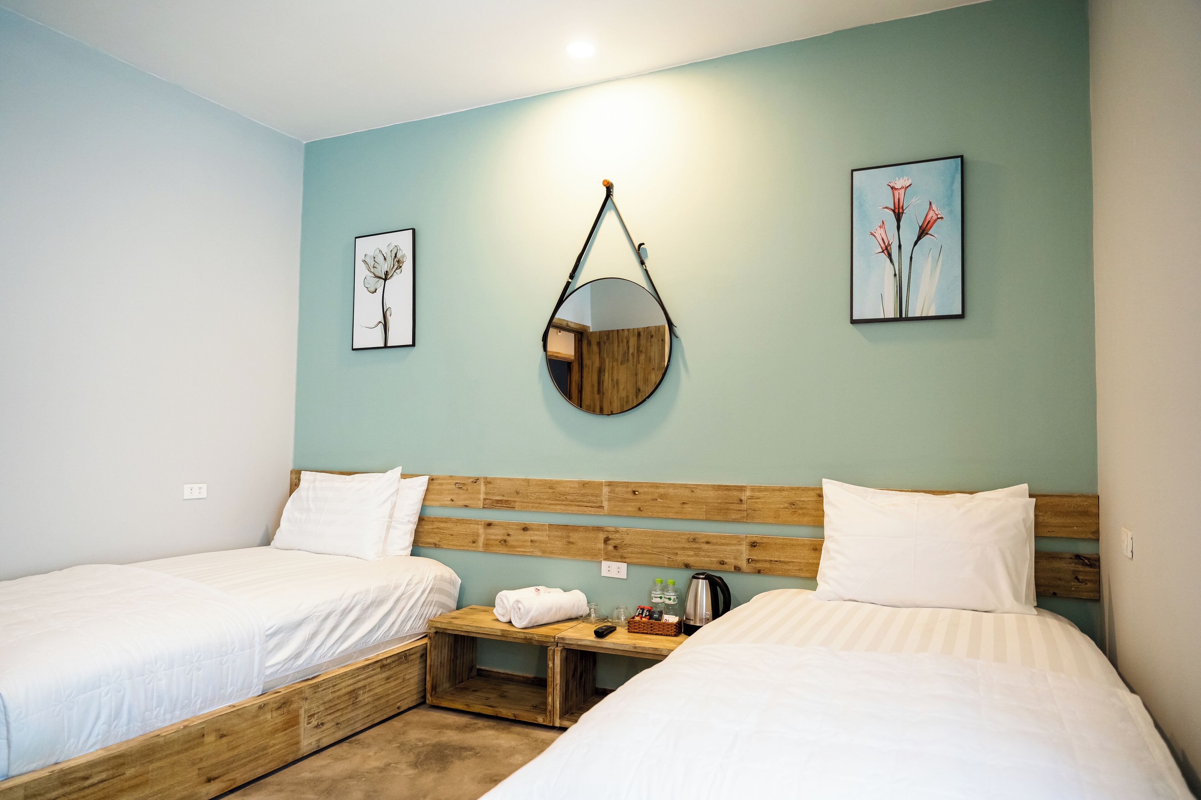 Una habitación doble con dos camas, cabecero de madera, mesita de noche con hervidor y cuadros en las paredes.
