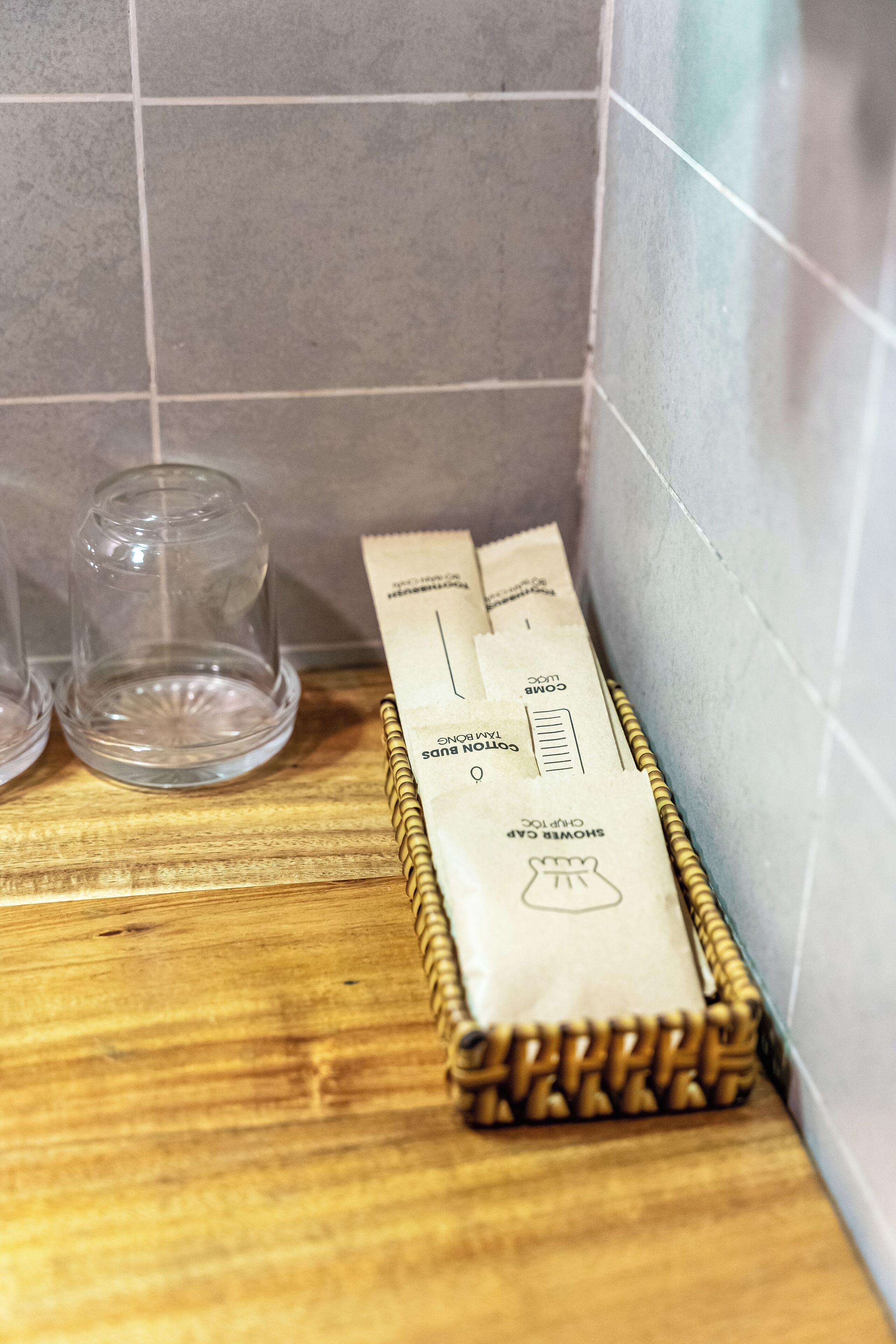 Een houten dienblad met zakjes met de tekst 'COLD BUN' en 'SHOWER GAC' tegen een betegelde muur.