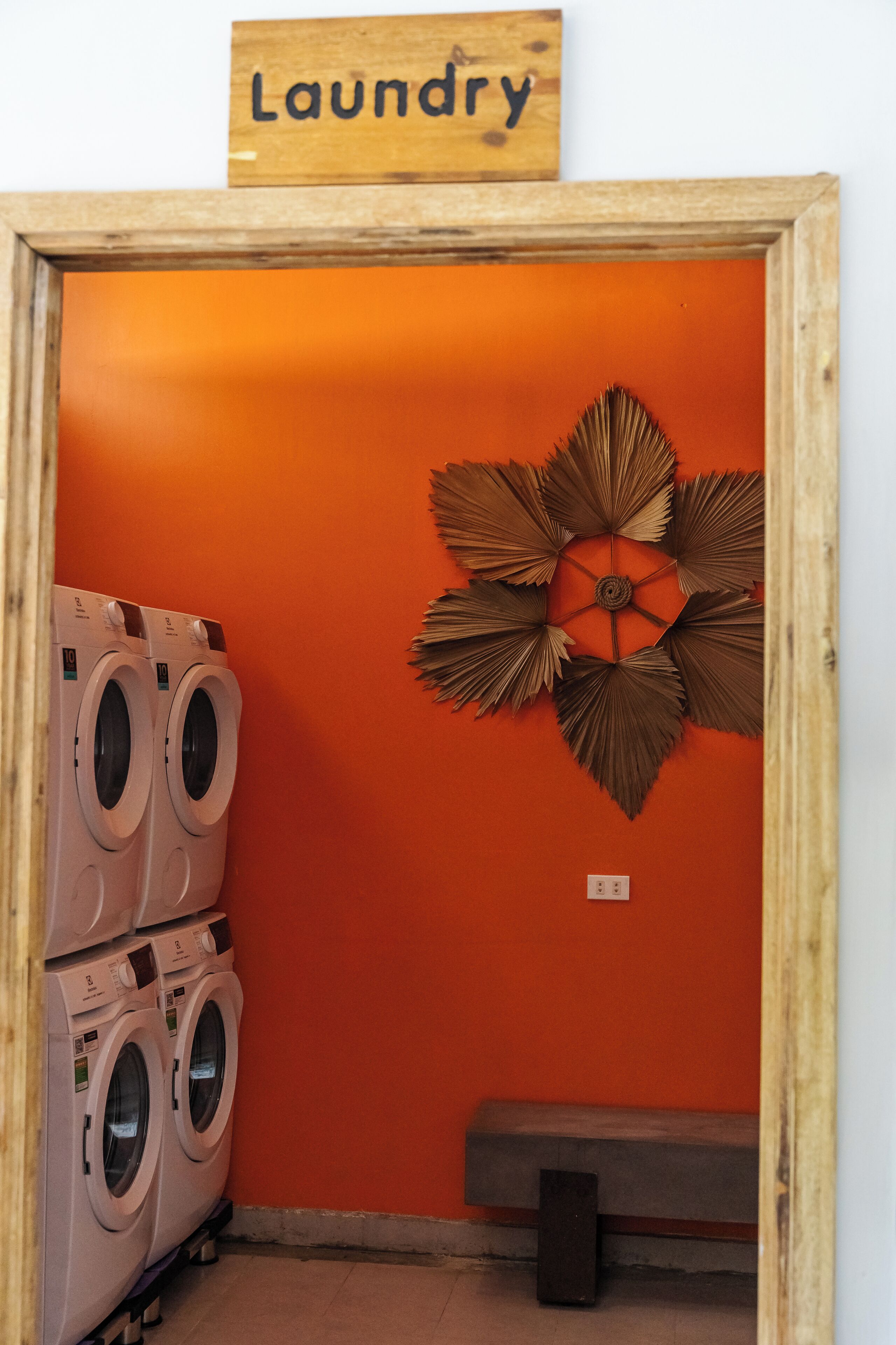 A laundry room with a sign above a door, a bench, and a decorative wall piece.