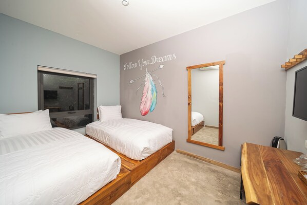 A bedroom with two beds, a wooden bench, a mirror, and a motivational wall art.