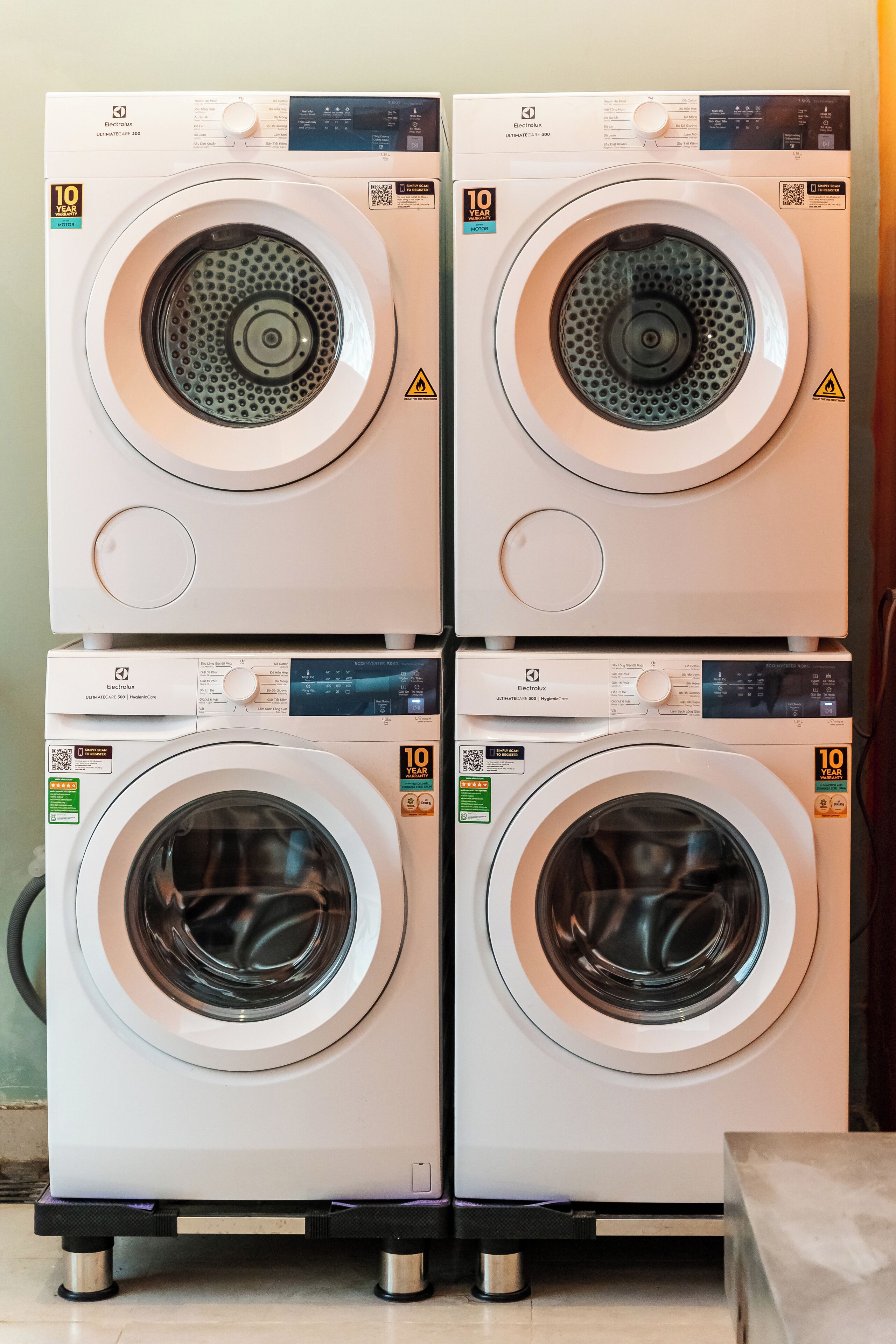 Quatre machines à laver à chargement frontal, empilées les unes sur les autres, avec panneaux de commande et étiquettes de sécurité.