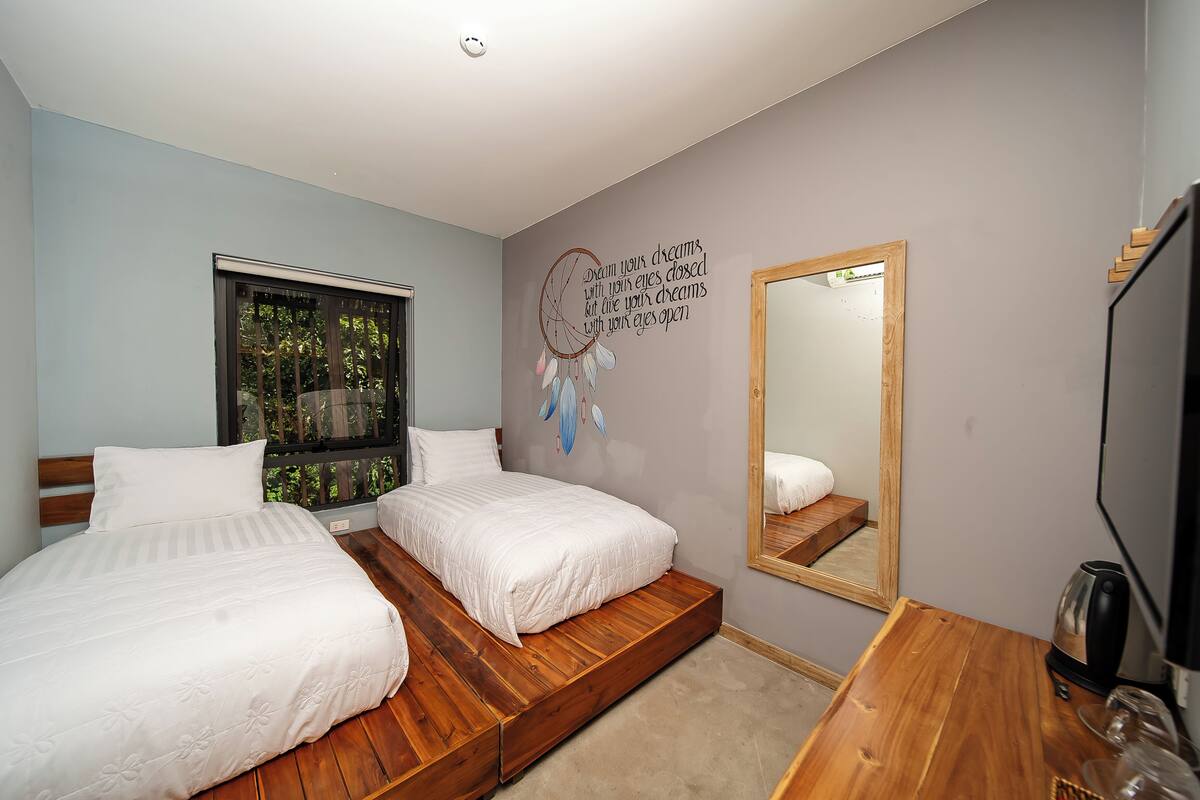 A bedroom with two beds, a wooden floor, a large mirror, and a dreamcatcher on the wall.