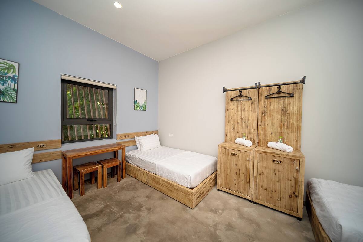 A bedroom with a wooden bed, a wooden desk, a bench, a wardrobe, and a window with a view of trees.