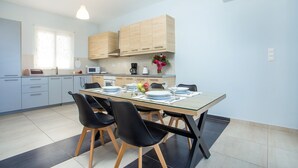 A modern kitchen with wooden cabinets, a dining table set for four, and a built-in microwave. - Rhodes Sea Villas (Rhodes)