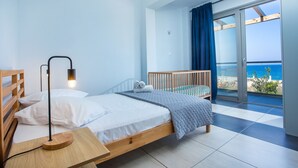 A bedroom with a bed, bedside table, lamp, and a view of the sea through a balcony. - Rhodes Sea Villas (Rhodes)