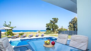 A poolside area with lounge chairs, a table with fruit, and a view of the ocean. - Rhodes Sea Villas (Rhodes)