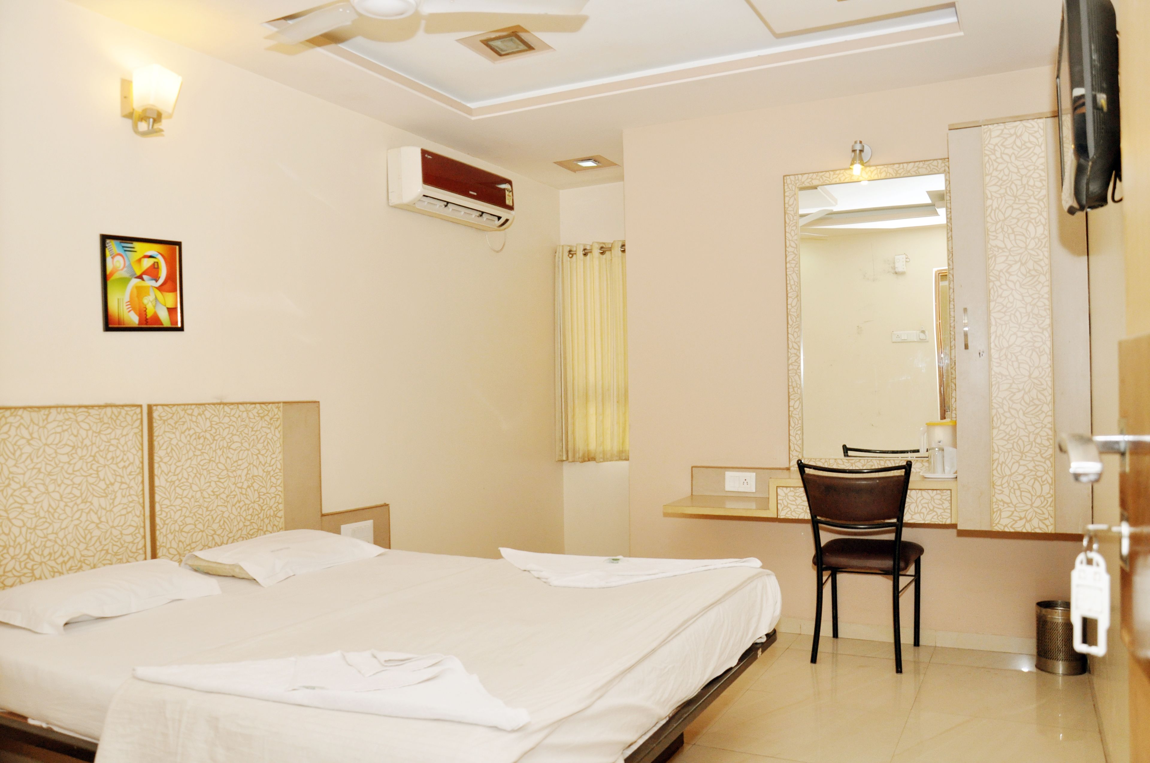 Quarto de hotel com duas camas, uma escrivaninha, uma cadeira, ar condicionado, um espelho e um quadro na parede.