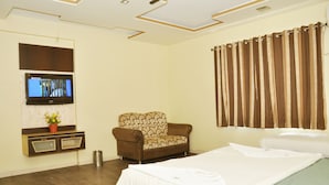 A hotel room with a bed, a sofa, a television mounted on the wall, and a curtain. - Hotel Sai Suraj Palace (Rahata)