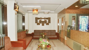 A lobby with a patterned sofa, a coffee table with flowers, and a reception desk. - Hotel Sai Suraj Palace (Rahata)