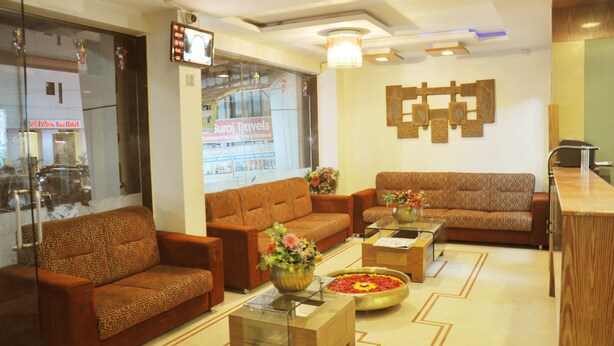 A modern hotel lobby with patterned sofas, a reception desk, and a large window displaying a hotel sign. - Hotel Sai Suraj Palace (Rahata)