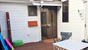 Una terraza de madera con una mesa, sillas, una puerta y un ventanal pequeño.