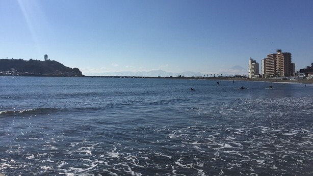 Vista costera con edificios, un muelle y surfistas.