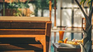 A wooden bench with a table beside it, a glass of orange juice, and a plate with food. - Sisikirana Villa (Unawatuna)